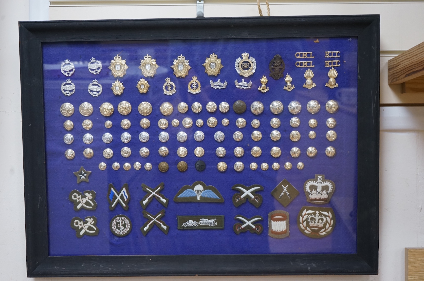 Two display cases containing military cap badges, buttons and shoulder titles, including; the Royal Medical Corps, the Royal Tank Regiment, the Royal Corps of Signals, the Royal Electrical and Mechanical Engineers, etc.